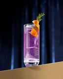 Purple cocktail in a tall glass with an orange twist and rosemary on a dark background